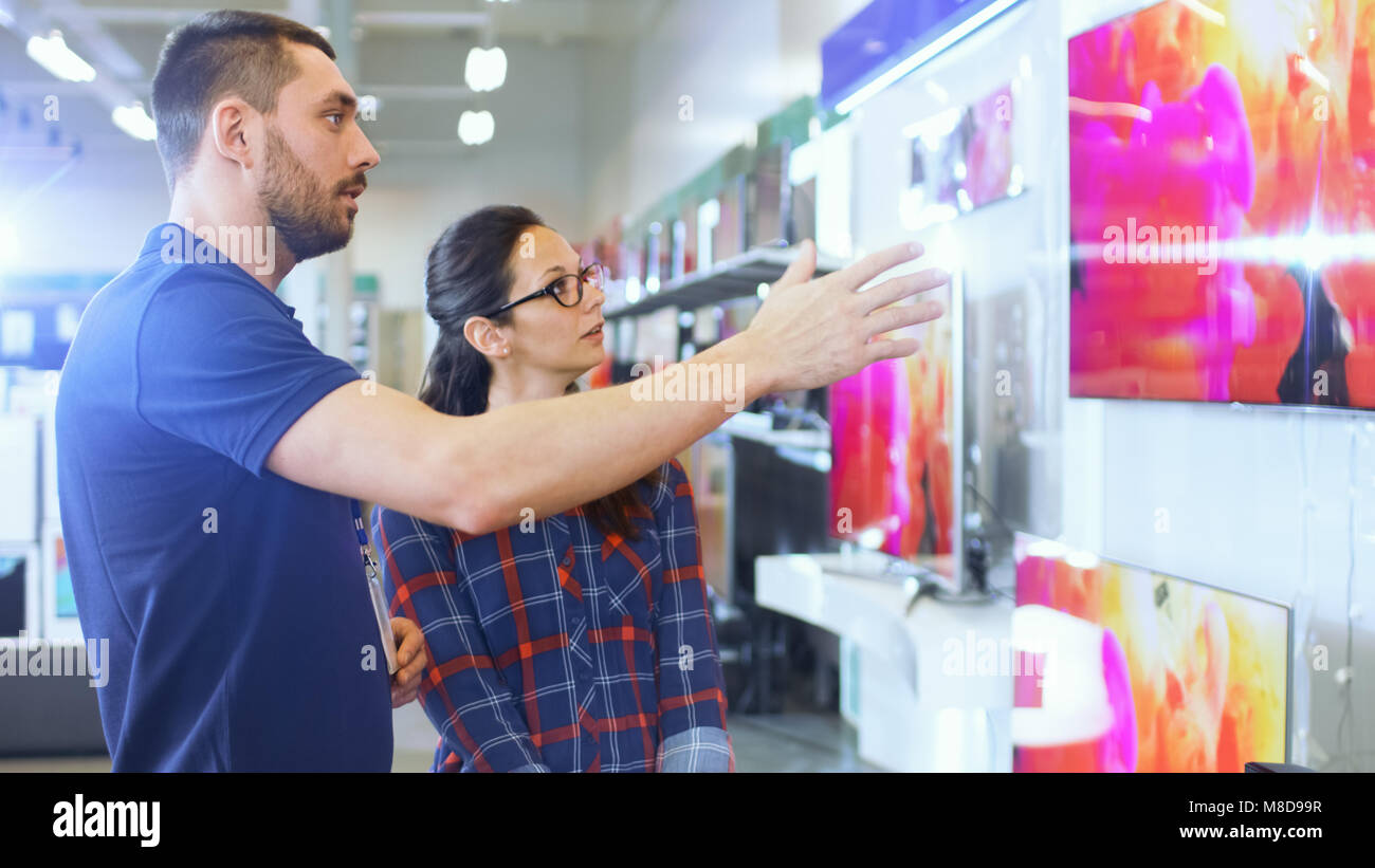 In the Electronics Store Professional Consultant Provides Expert Advice to a Young Woman Who Looks for a  New 4K UHD TV to Buy. Stock Photo