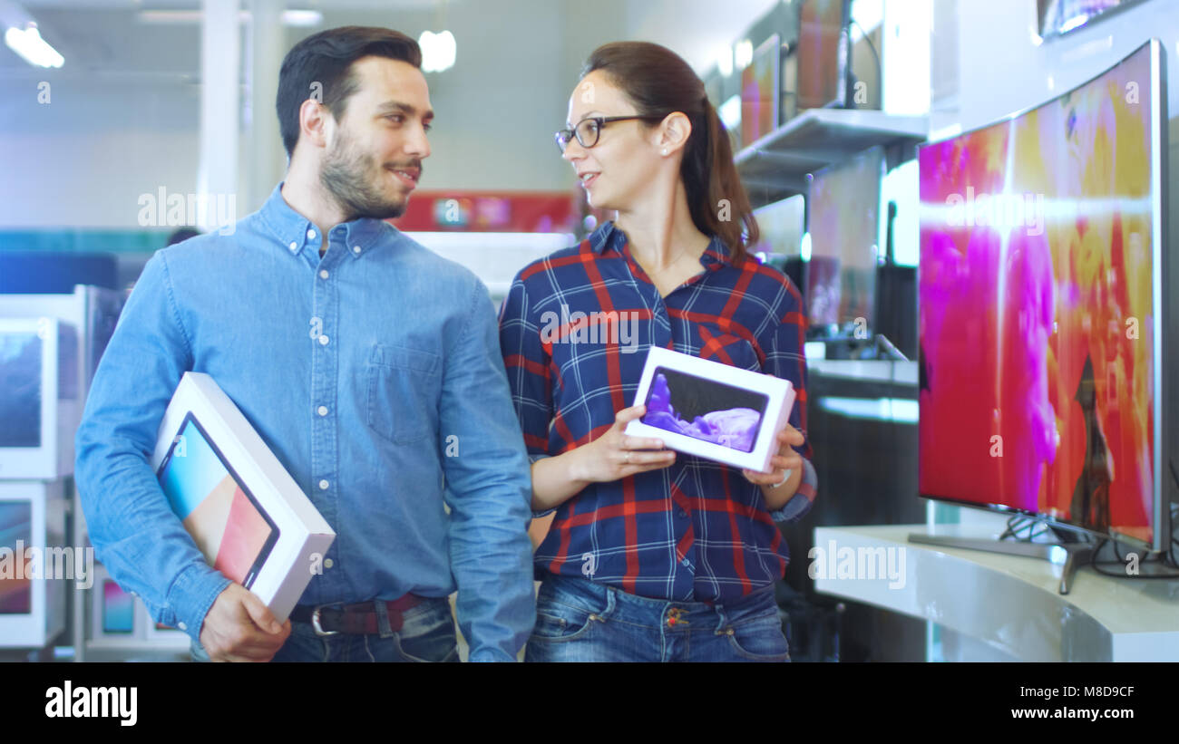 Happy Couple Walking In the Electronics Store, They've Purchased Latest Model of the Tablet Computer for Him and New Smartphone for Her. Stock Photo
