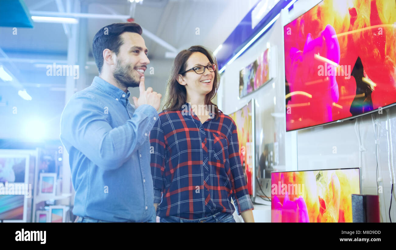 Young Couple Shopping for a New 4K TV Set in the Electronics Store. They're Trying to Decide on the Best Model But Have Doubts. Stock Photo