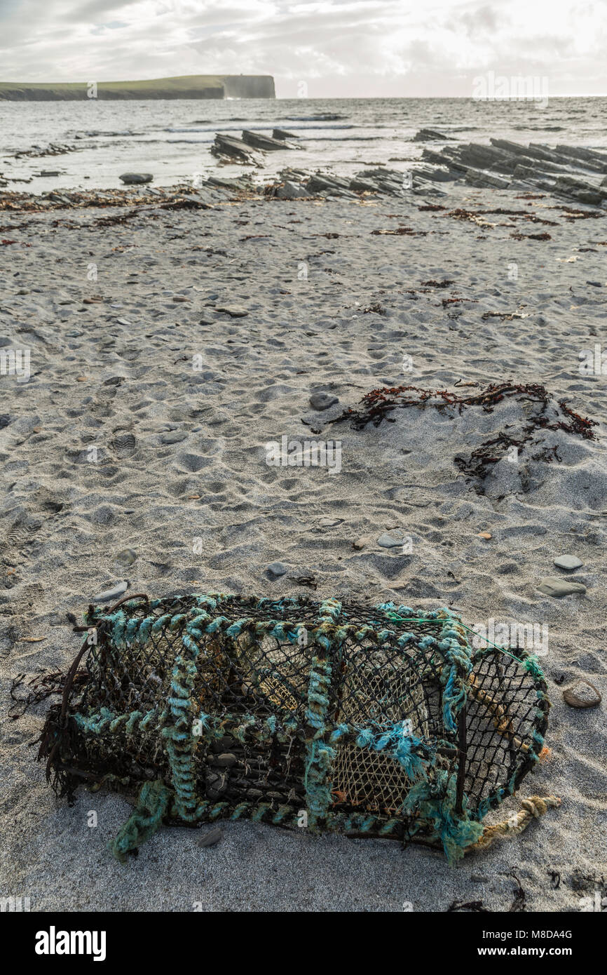 Abandoned vintage lobster pot or creel on the seashore with distant cliffs Stock Photo
