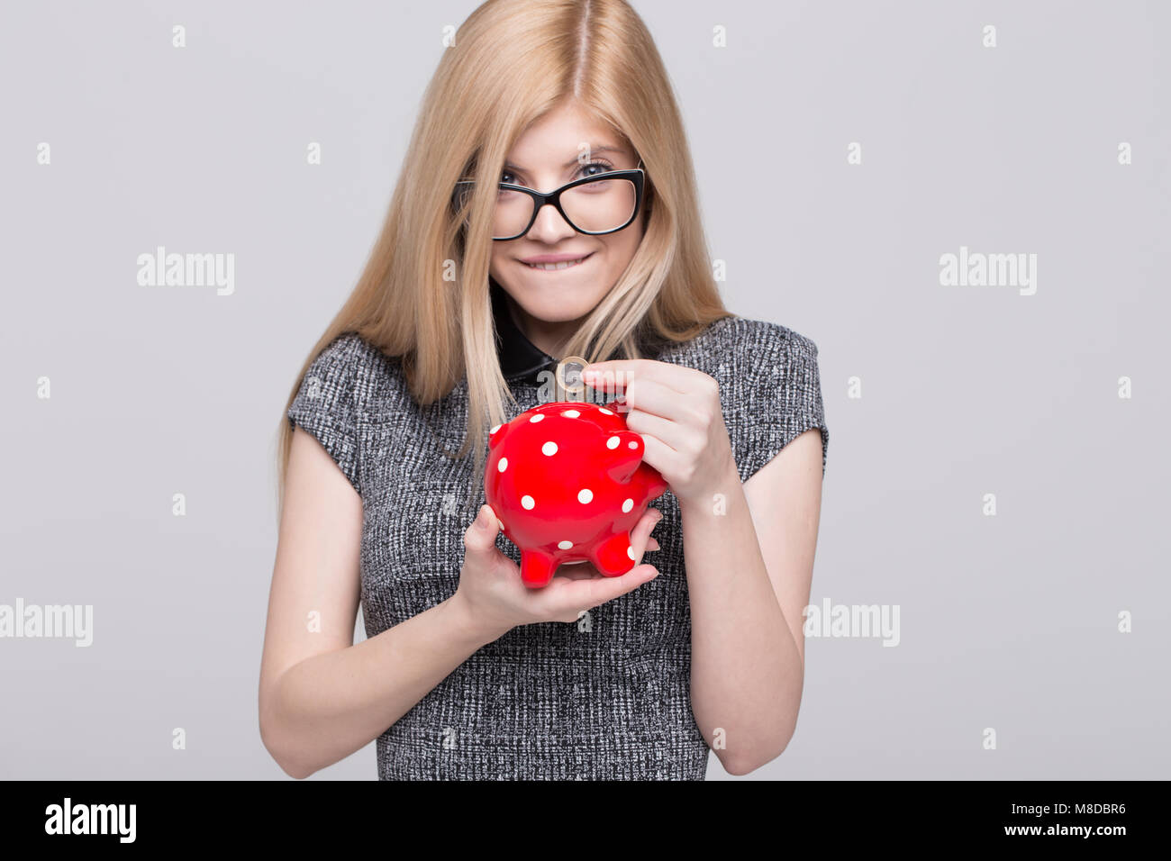 Young excited blonde woman put one euro into red dotted piggy bank, saving Stock Photo