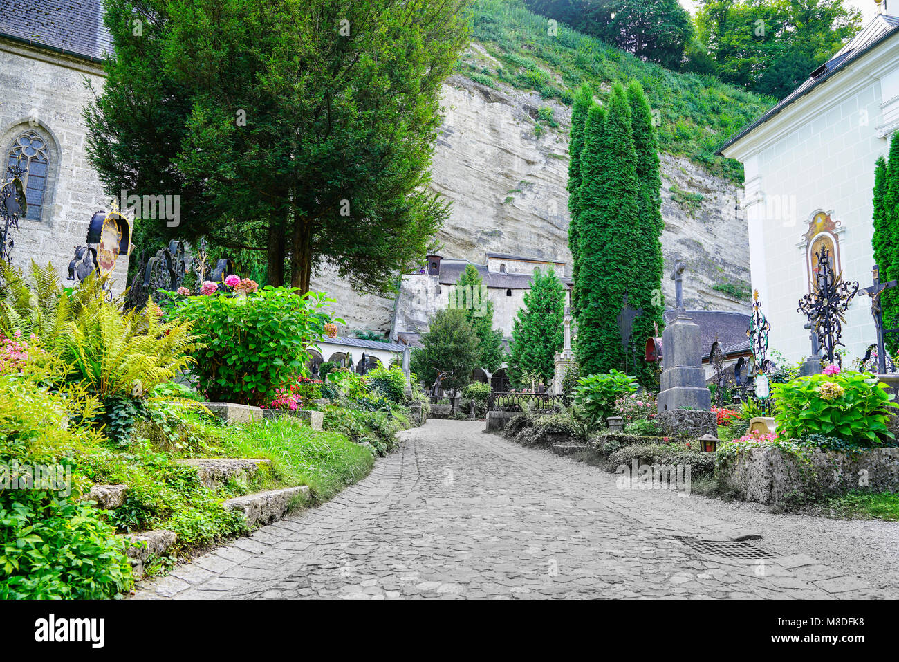 SALZBURG, AUSTRIA - SEPTEMBER 6 2017;  path between luxuriant cemetery gardens and graves and St. Peter's church Stock Photo