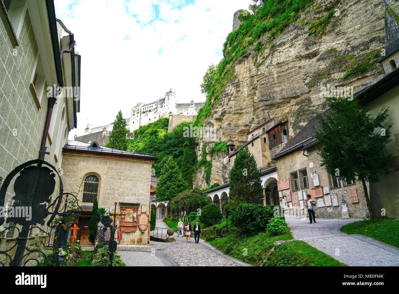 SALZBURG< AUSTRIA - SEPTEMBER 6 2017; Tourists on converging paths between luxuriant cemetery gardens and graves and St. Peter's church  with  Hohensa Stock Photo