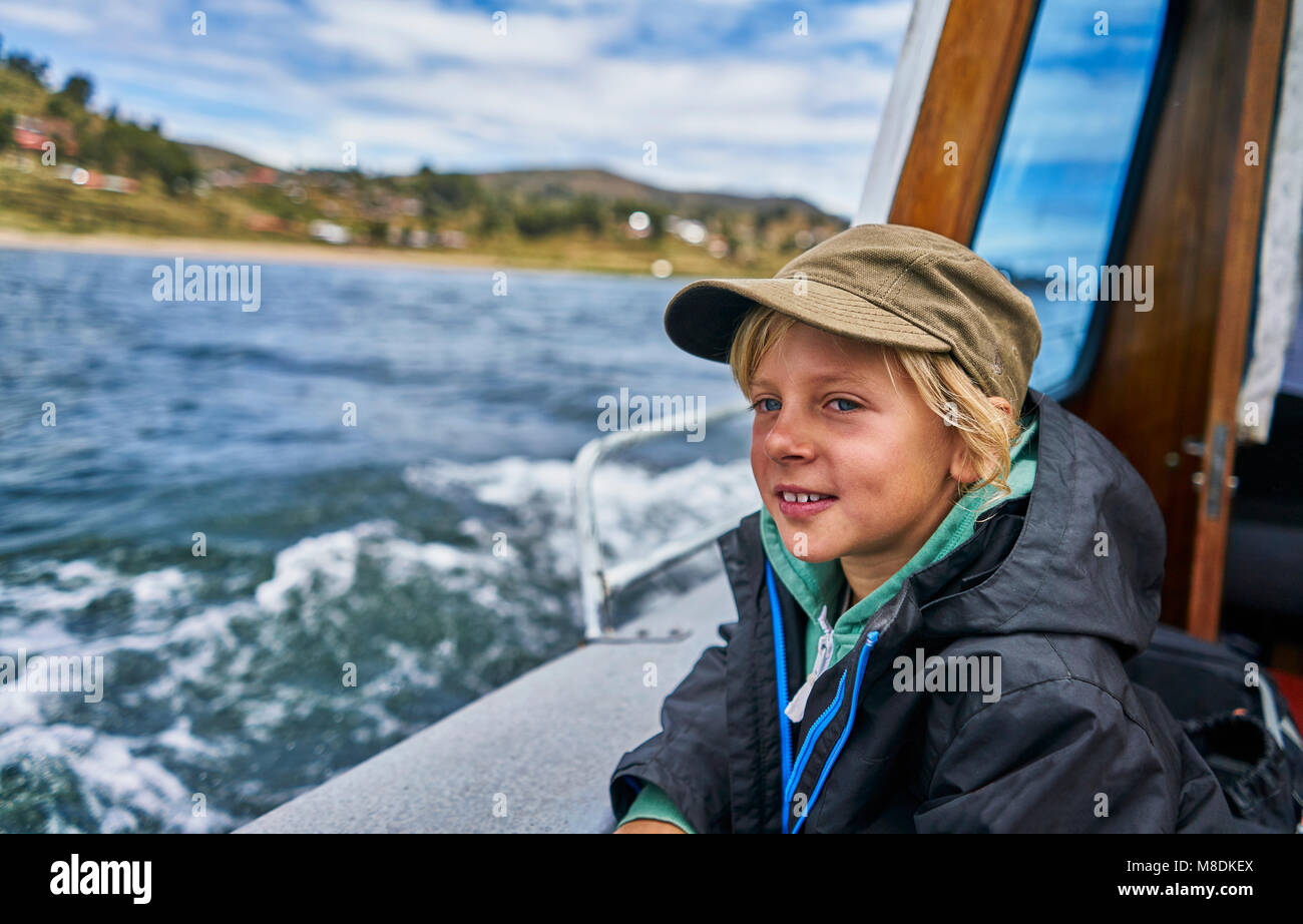 Boy looking out from motor boat at sea, Puno, Peru Stock Photo