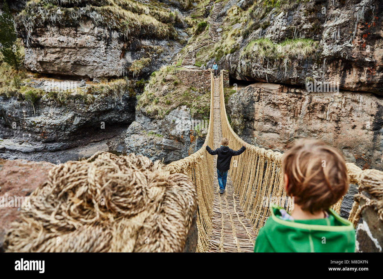Over shoulder view of boy, brother and mother crossing Inca rope bridge, Huinchiri, Cusco, Peru Stock Photo
