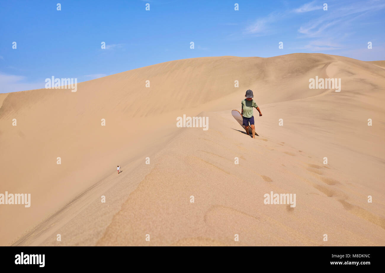 Boy with sandboard on sand dunes, Ica, Peru Stock Photo