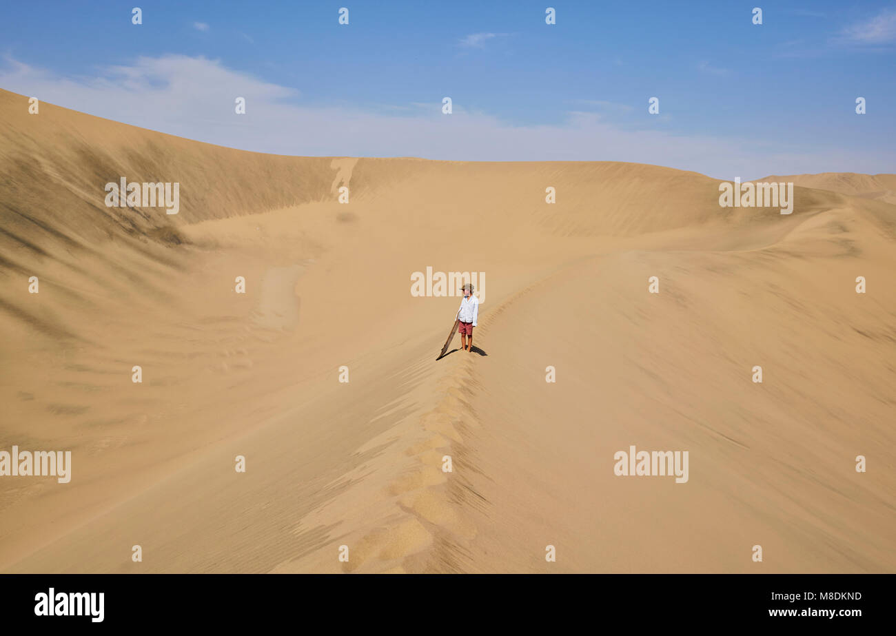 Boy with sandboard looking out over sand dunes, Ica, Peru Stock Photo