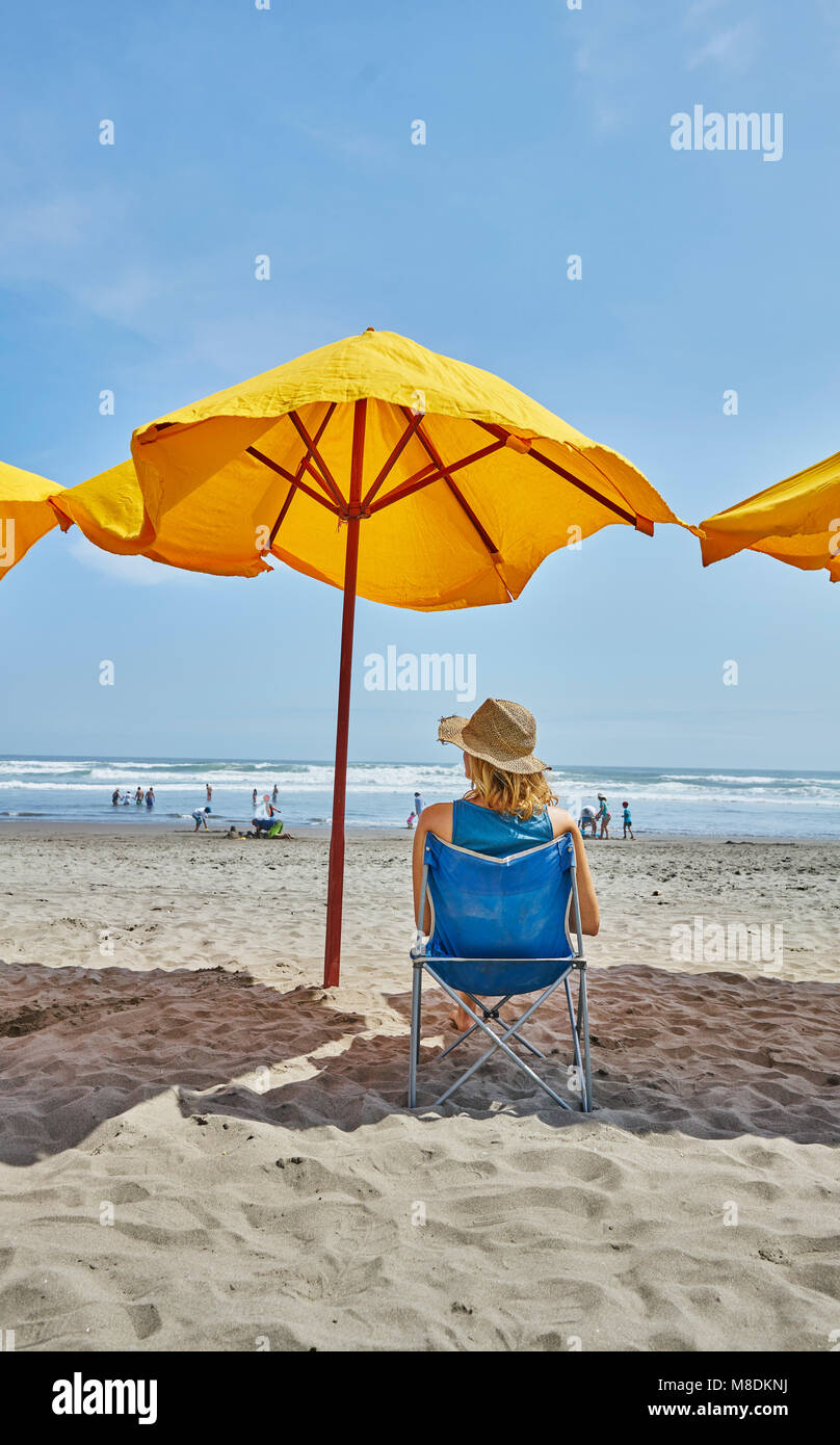 Rear view of female tourist sitting under beach umbrella, Camana, Arequipa, Peru Stock Photo