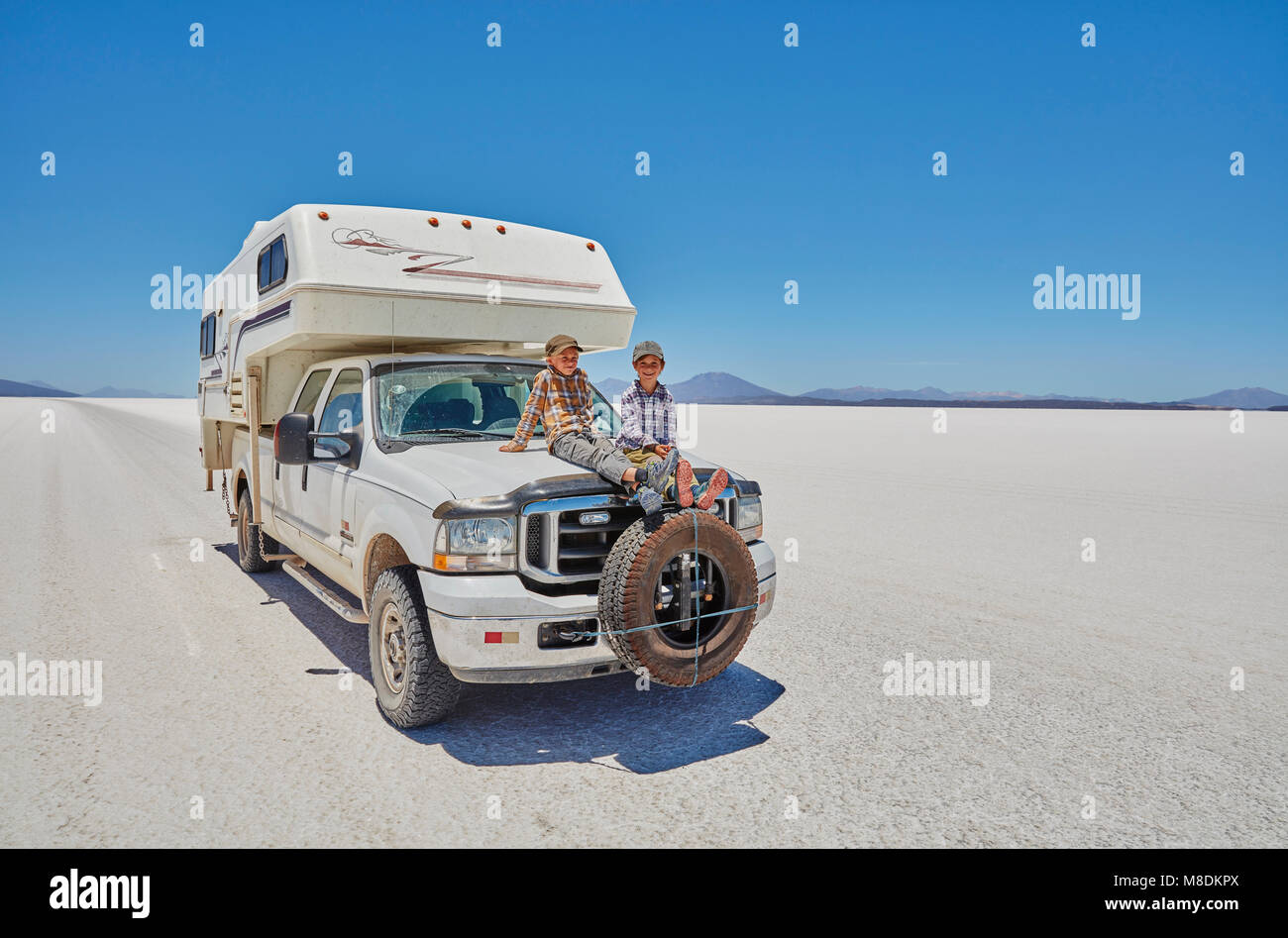 Two boys sitting on parked recreational vehicle, Salar de Uyuni, Uyuni, Oruro, Bolivia, South America Stock Photo