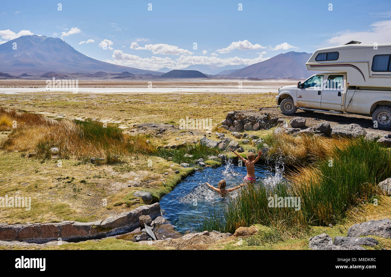Two boys playing in water pool beside parked recreational vehicle, Salar de Chiguana, Chiguana, Potosi, Bolivia, South America Stock Photo