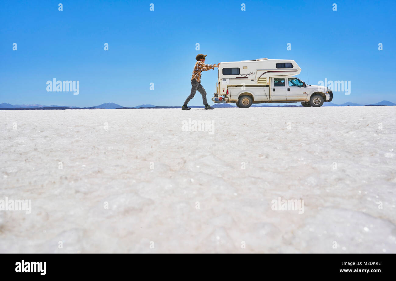 False perspective image of boy on salt flats, pretending to push vehicle, vehicle in background, Salar de Uyuni, Bolivia Stock Photo