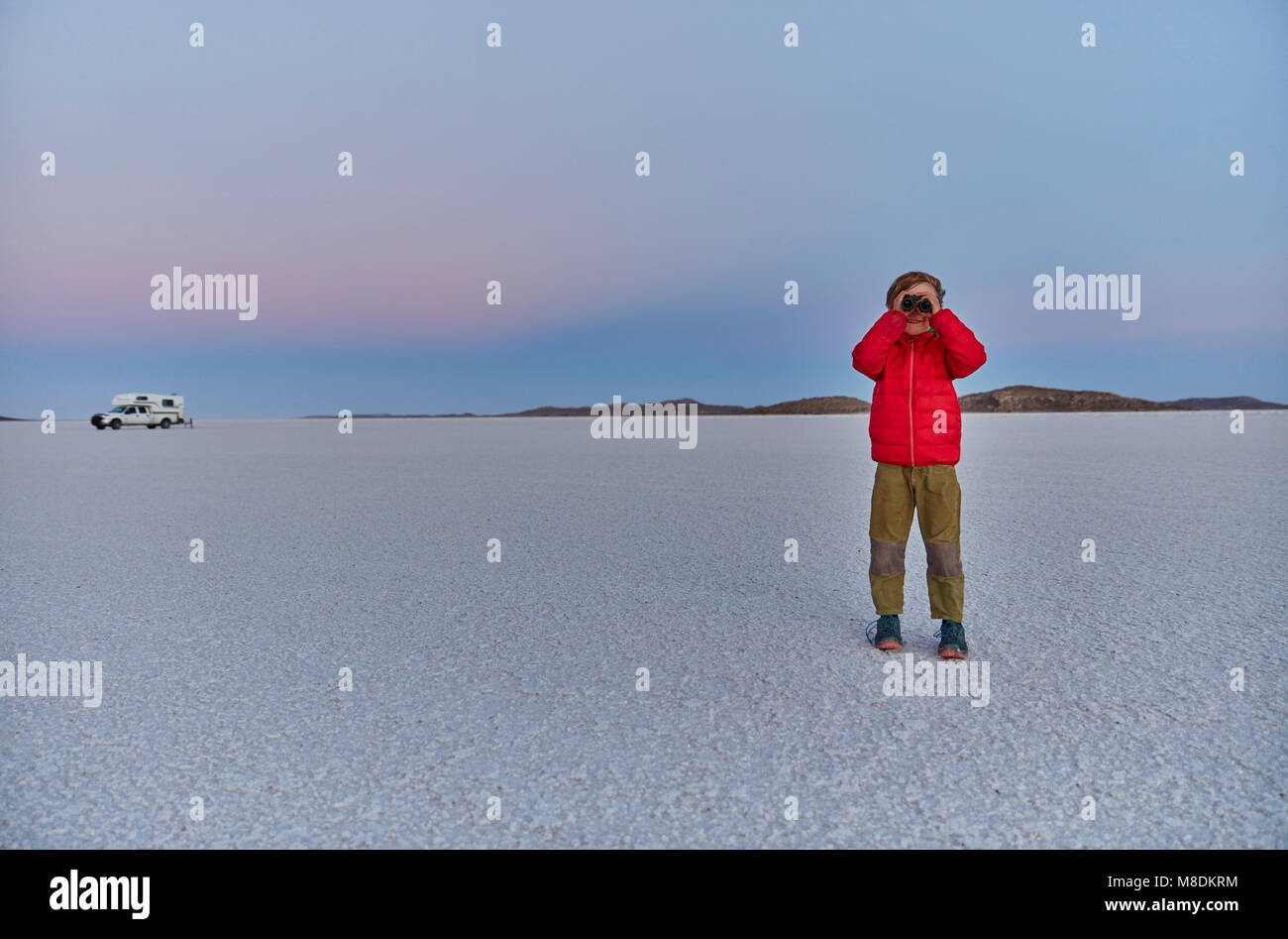 Young boy standing on salt flats, looking at view, recreational vehicle in background, Salar de Uyuni, Uyuni, Oruro, Bolivia Stock Photo