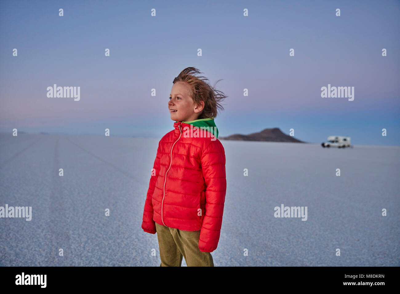 Young boy standing on salt flats, looking at view, recreational vehicle in background, Salar de Uyuni, Bolivia, South America Stock Photo