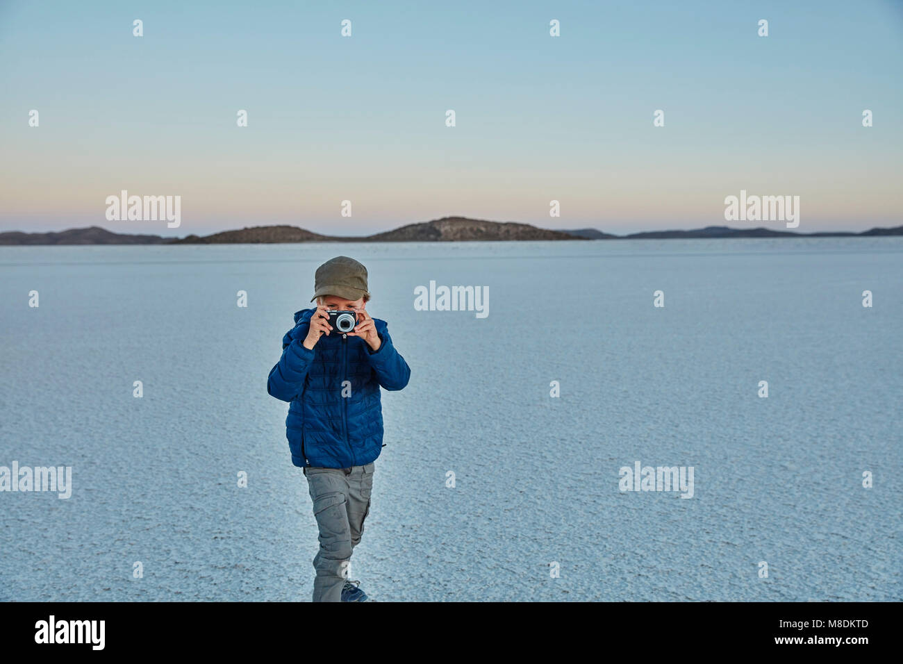 Young boy standing on salt flats, looking through camera, Salar de Uyuni, Uyuni, Oruro, Bolivia, South America Stock Photo