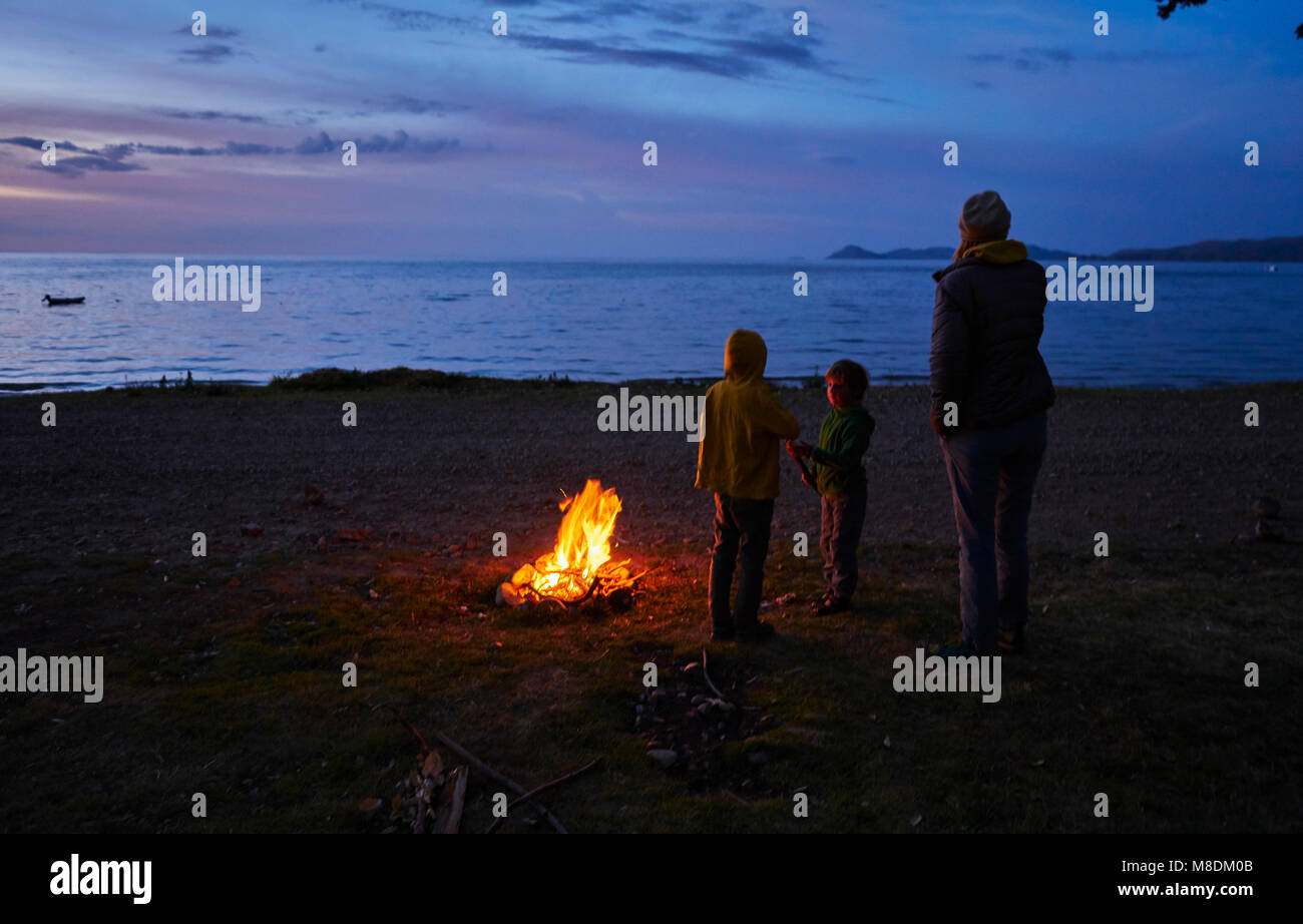 Mother and sons beside camp fire, looking at lake view, rear view, Copacabana, Oruro, Bolivia, South America Stock Photo