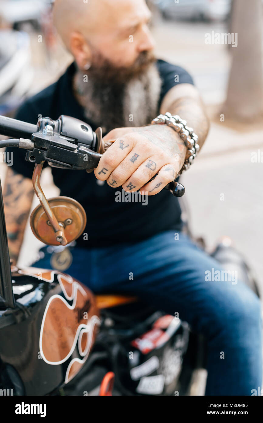 Mature male hipster astride motorcycle, close up of tattooed hand Stock Photo