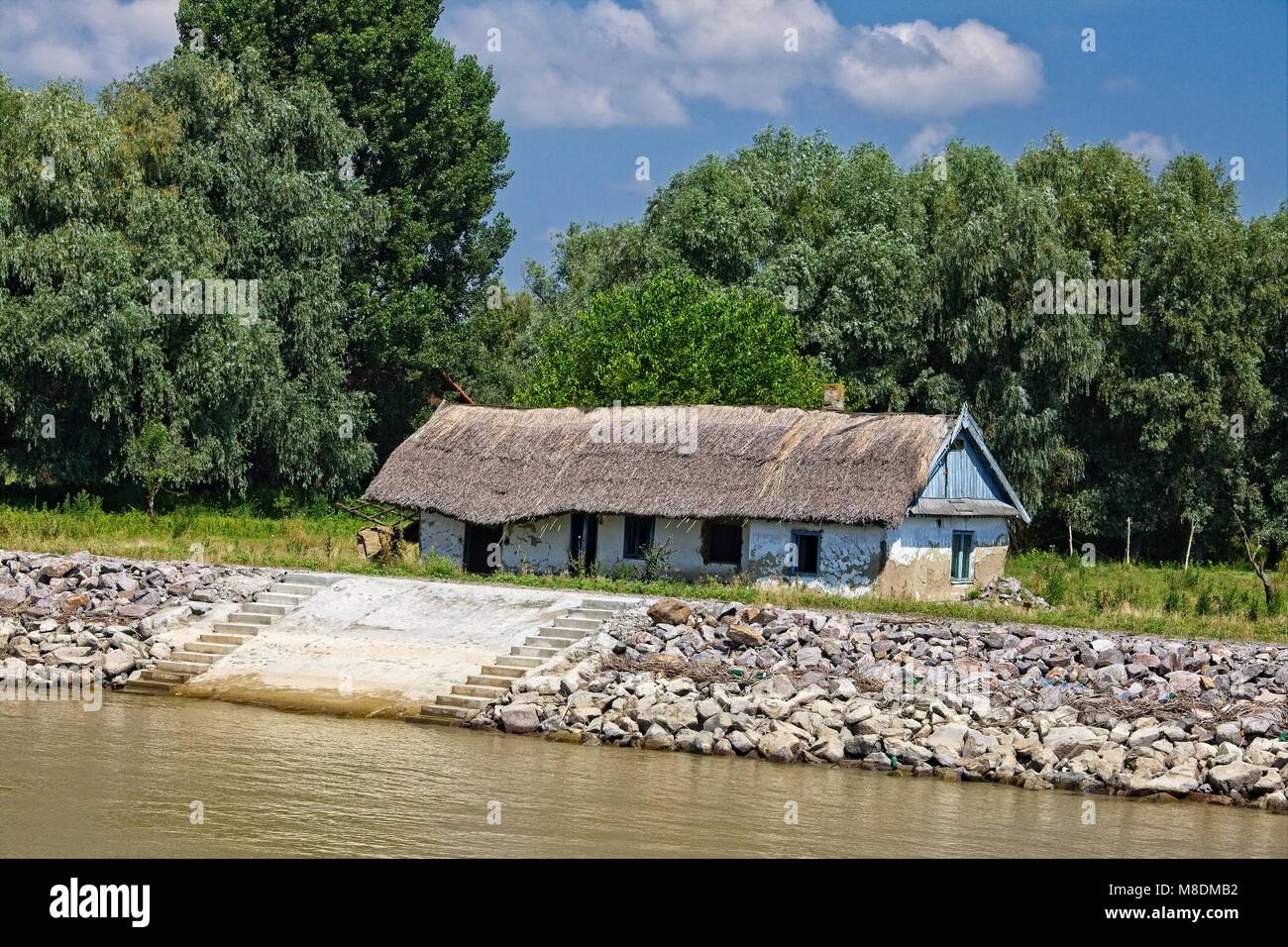 TRADITIONAL THATCHED FARMHOUSE AND RIVER BANK FLOOD PROTECTION DOWNSTREAM OF TULCEA ON THE DANUBE RIVER DELTA Stock Photo