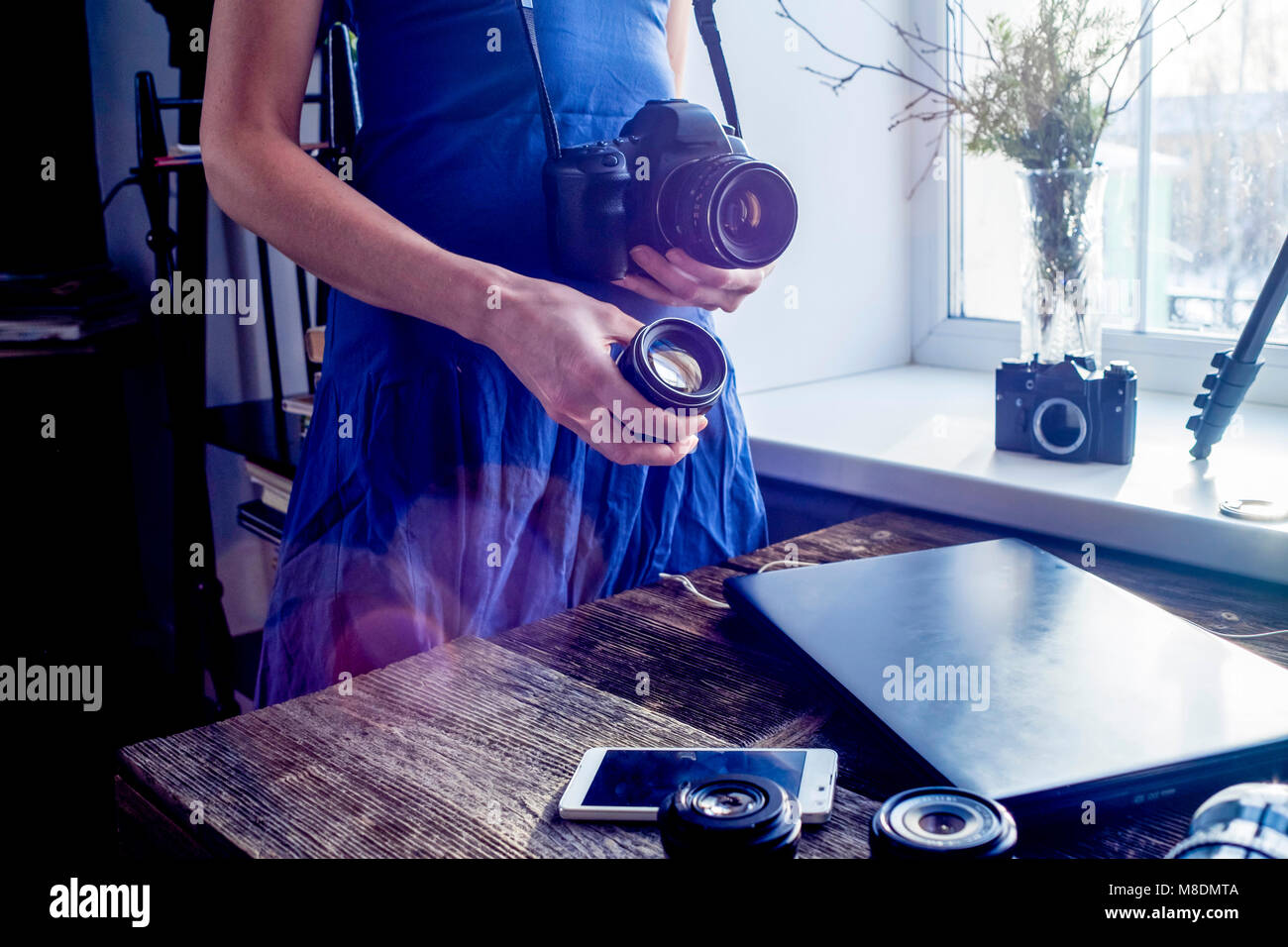 Mid adult woman, standing beside window, holding camera and camera lens Stock Photo