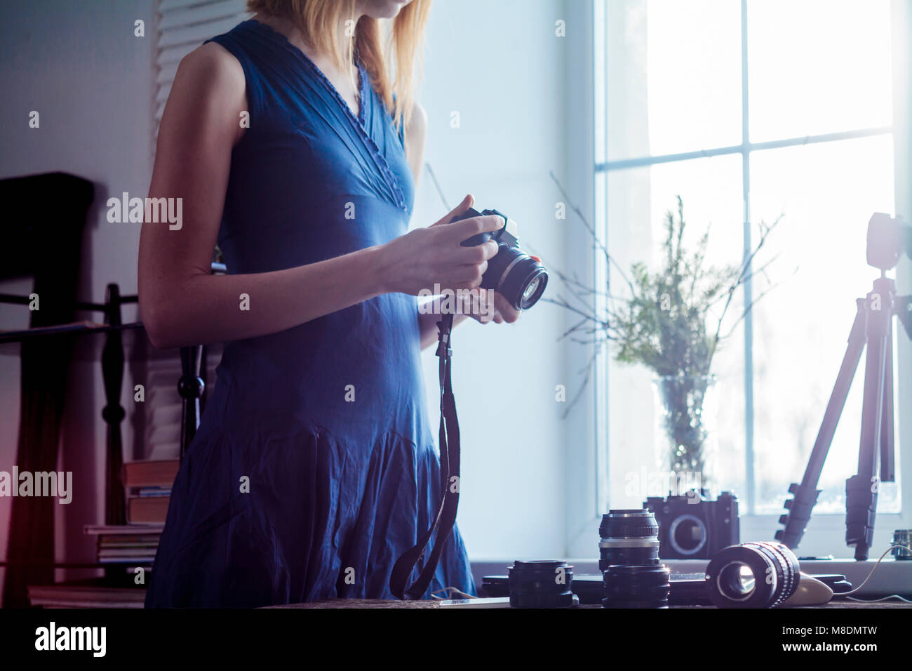Mid adult woman, beside window, holding camera, camera lenses on table in front of her, mid section Stock Photo