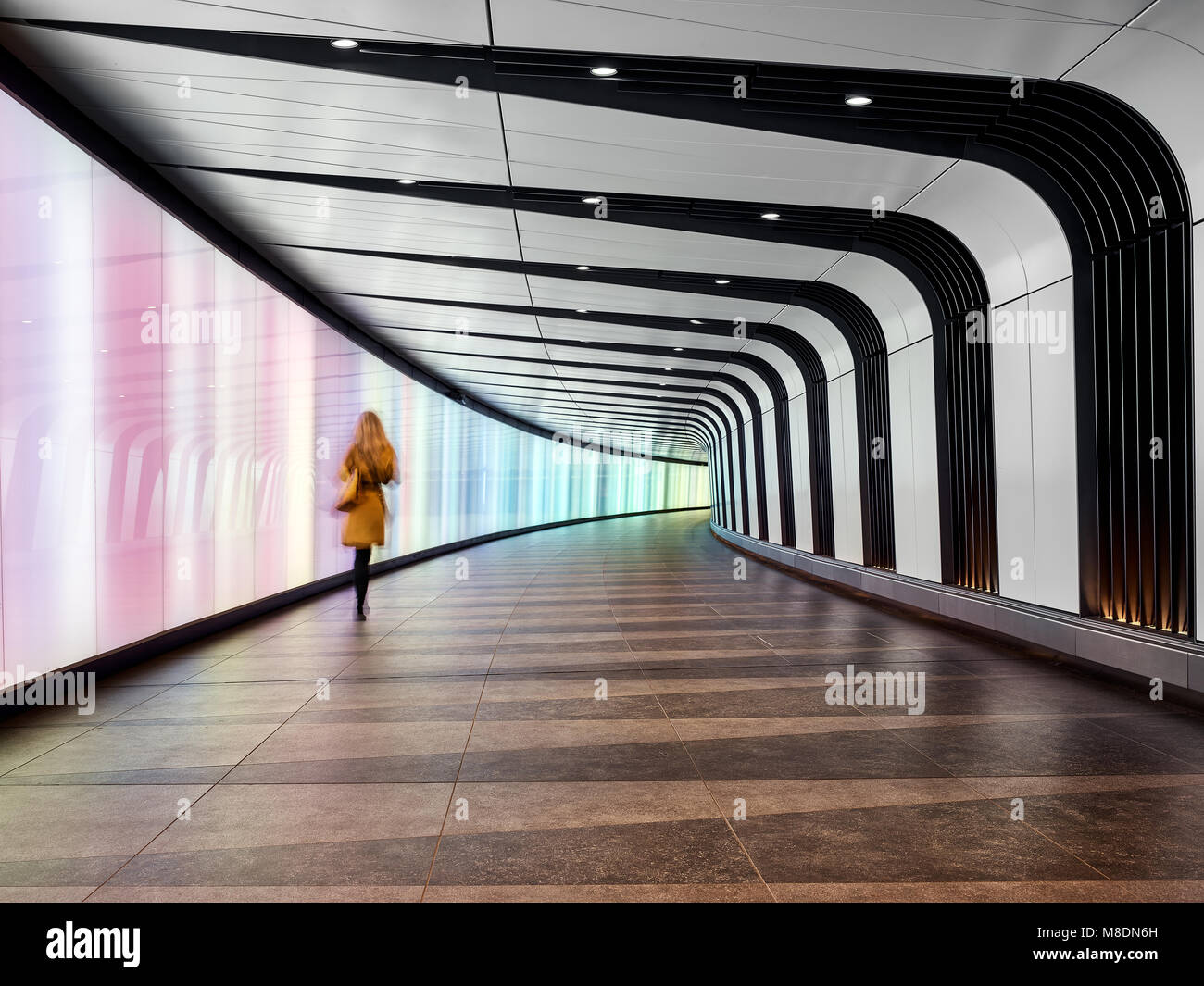 Rear view of woman walking through tunnel walkway, London City Airport, London, UK Stock Photo