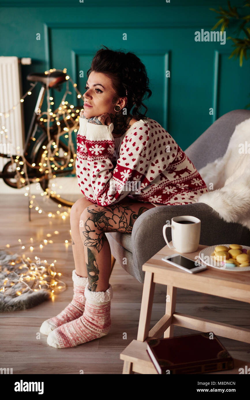 Young woman sitting at home, wearing christmas jumper, thoughtful expression Stock Photo