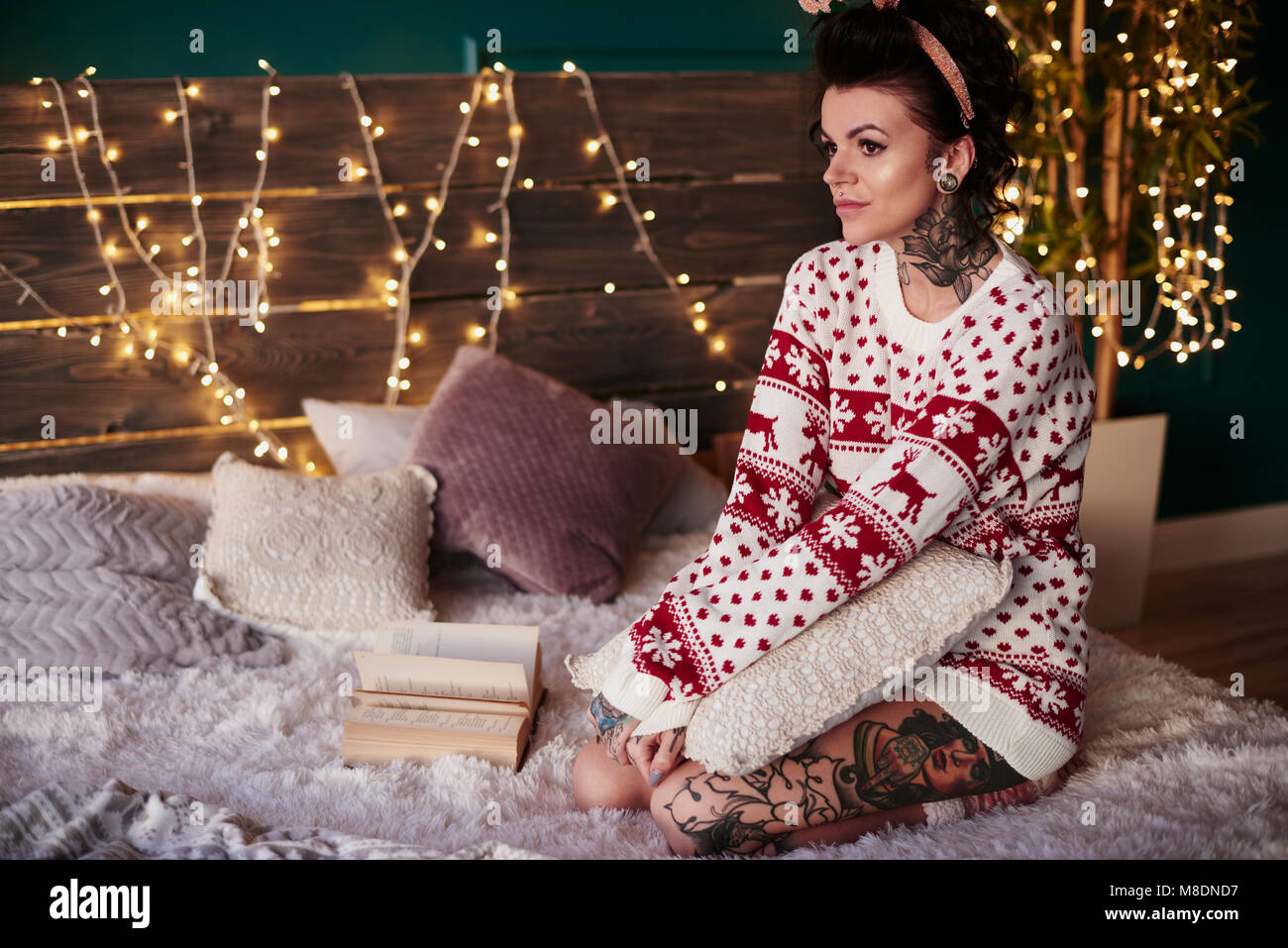 Young woman sitting on bed, wearing christmas jumper, thoughtful expression Stock Photo