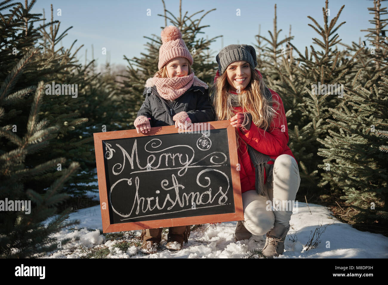 Girl and mother in christmas tree forest with merry christmas sign, portrait Stock Photo