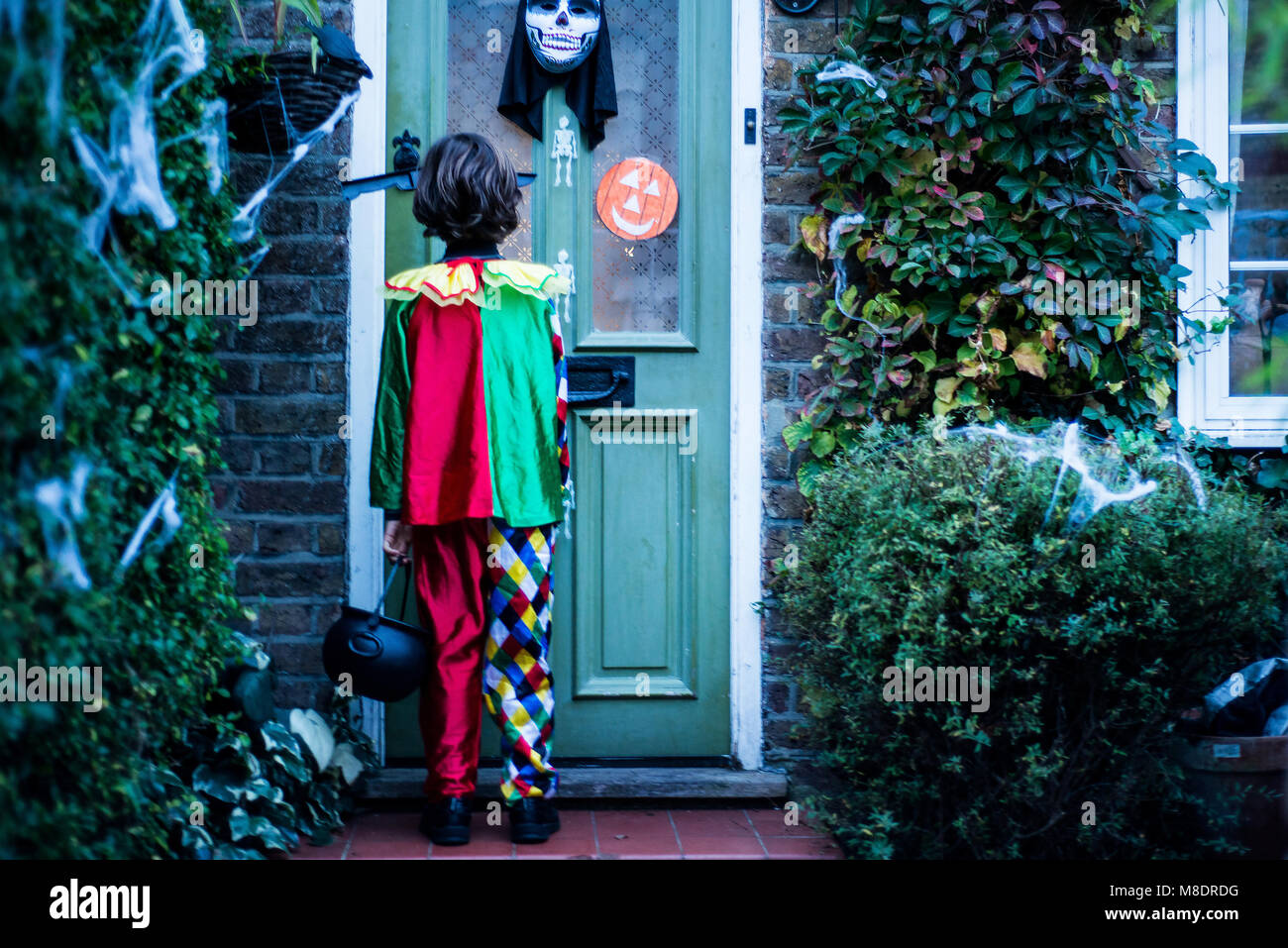 Young boy in halloween costume, standing at door, trick or treating, rear view Stock Photo