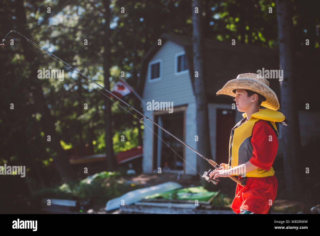 Boy in cowboy hat fishing from lakeside Stock Photo