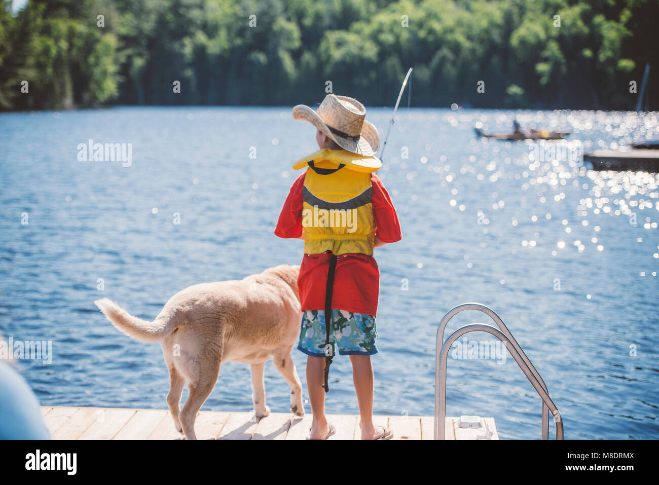 Rear view of dog and boy in cowboy hat fishing from lake pier