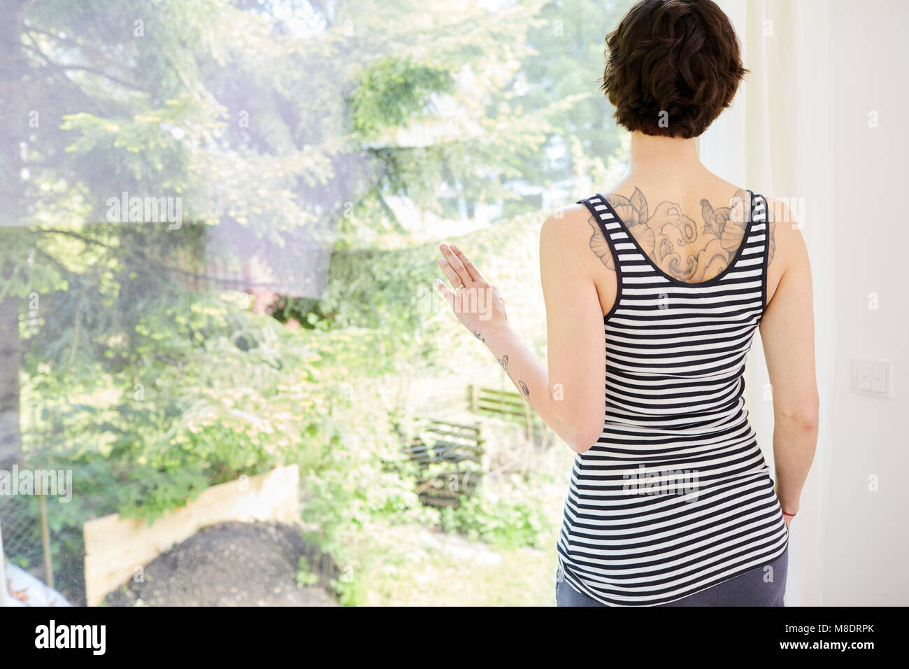 Mid adult woman, at home, looking out of window, rear view Stock Photo