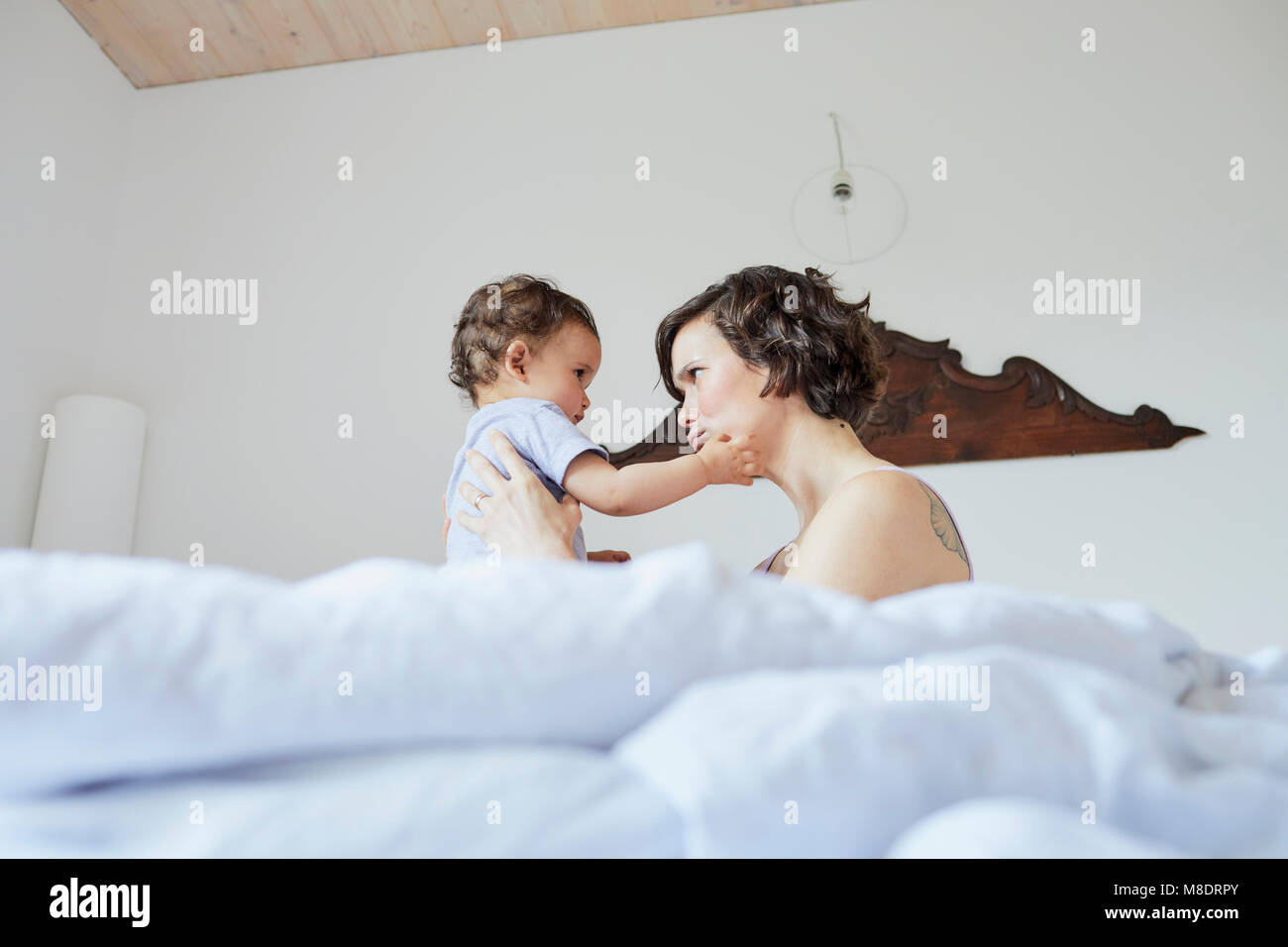 Mother sitting in bed with baby girl, face to face, pensive expression Stock Photo