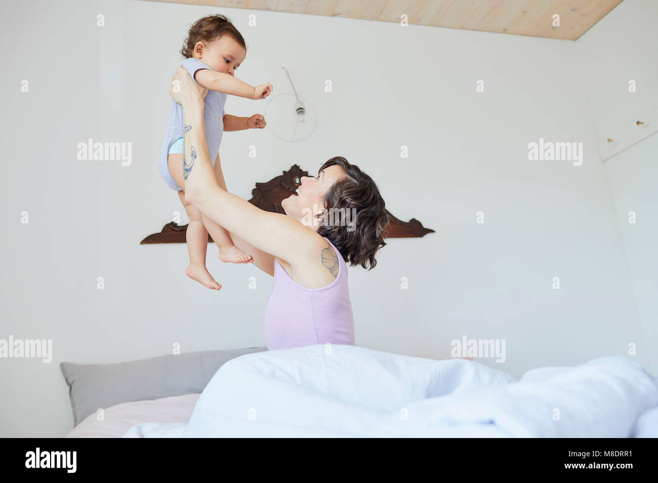 Mother sitting in bed, holding baby girl in air, smiling Stock Photo