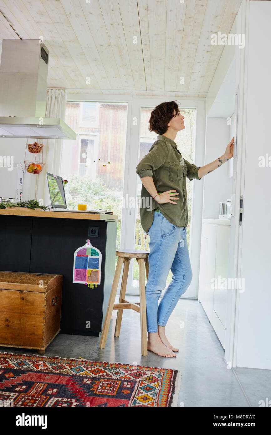Mid adult woman looking at planner on kitchen wall Stock Photo