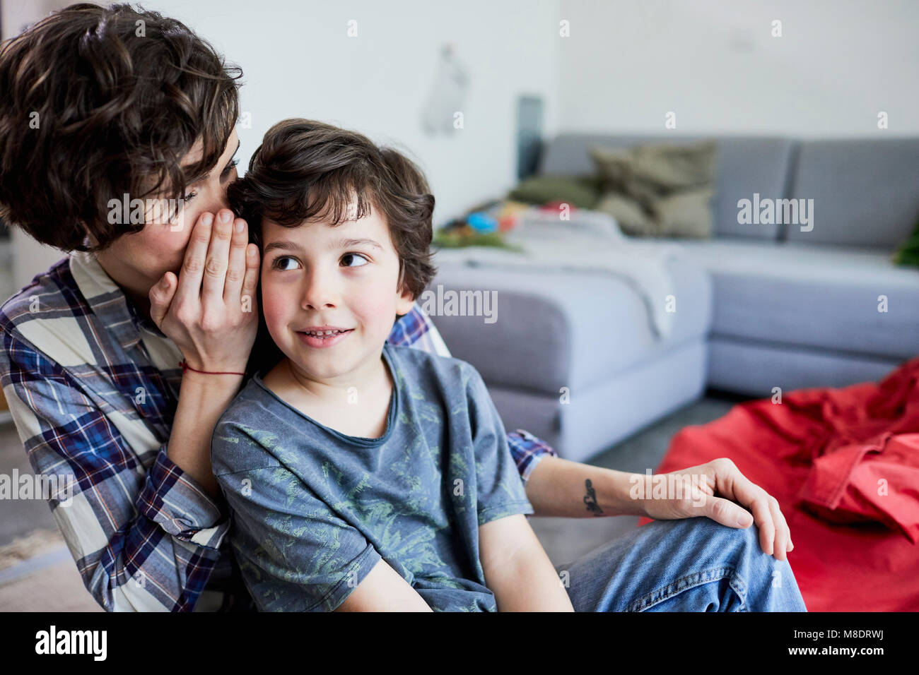 Mother and son at home, mother whispering into son's ear Stock Photo