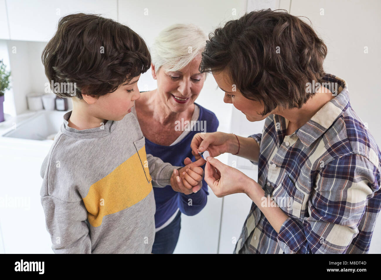 Mother putting plaster on son's finger, grandmother holding grandson's hand Stock Photo