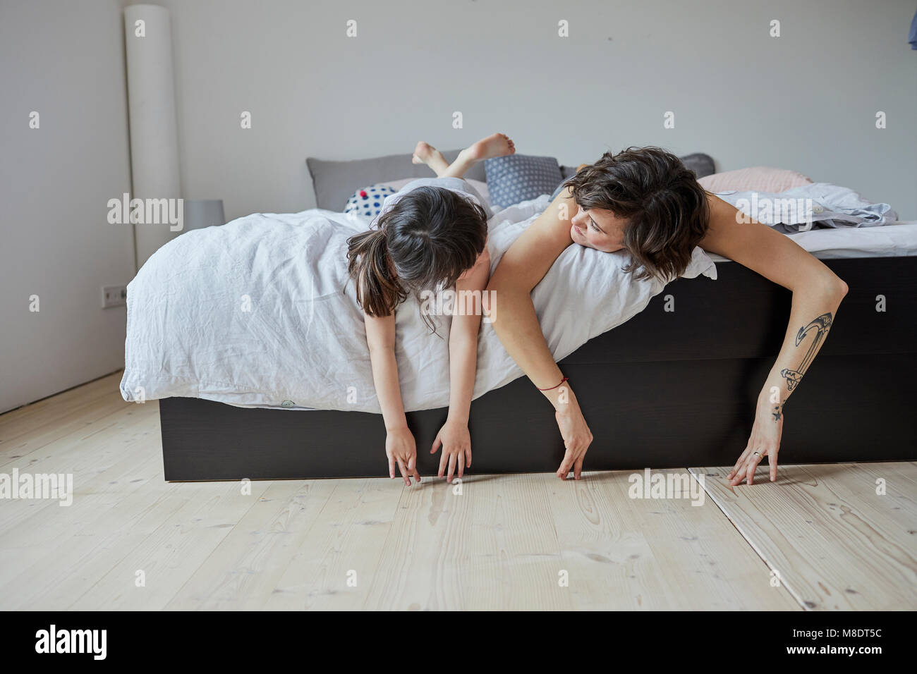 Mother and daughter lying on bed, hands touching floor Stock Photo