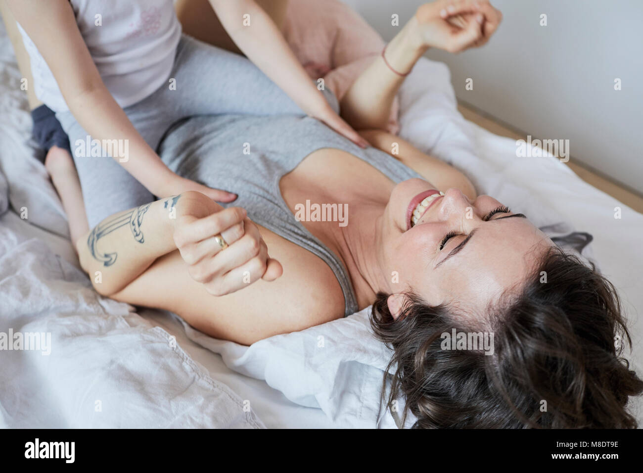 Mother and daughter lying on bed, fooling around, laughing, mid section Stock Photo