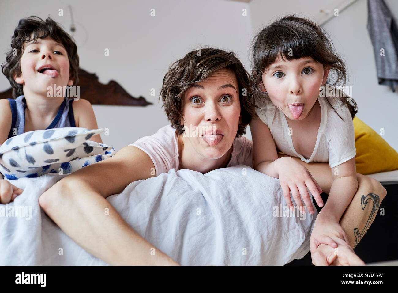 Portrait of mother, son and daughter, lying on bed, poking tongue out Stock Photo