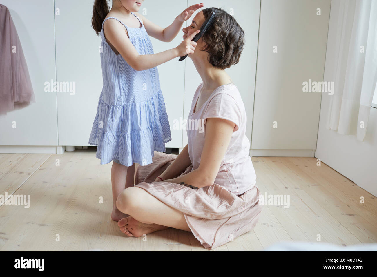 Mother sitting on floor, daughter brushing mother's hair, mid section Stock Photo