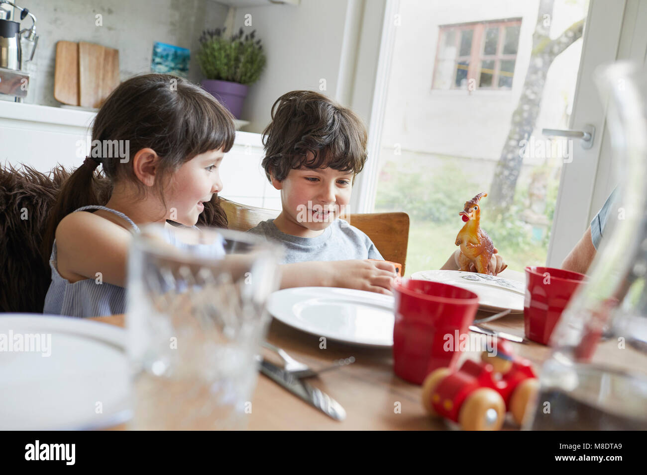 Young boy and girl sitting at dinner table, smiling Stock Photo