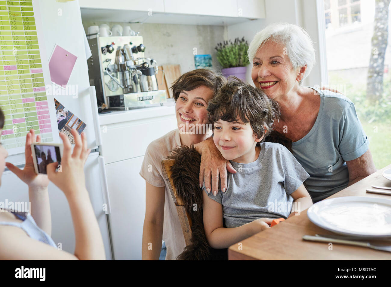Young girl photographing, brother, mother and grandmother, using smartphone Stock Photo