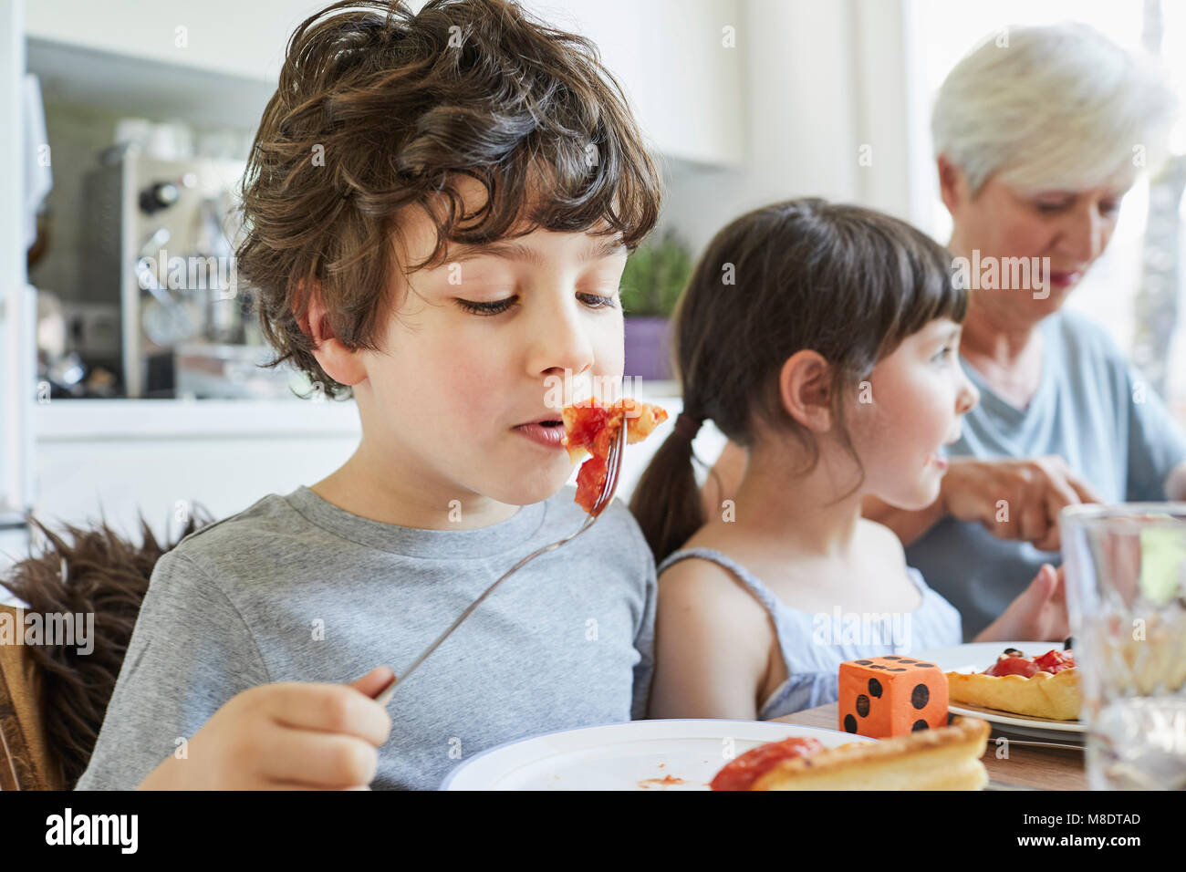 Young boy eating lunch at table with sister and grandmother Stock Photo