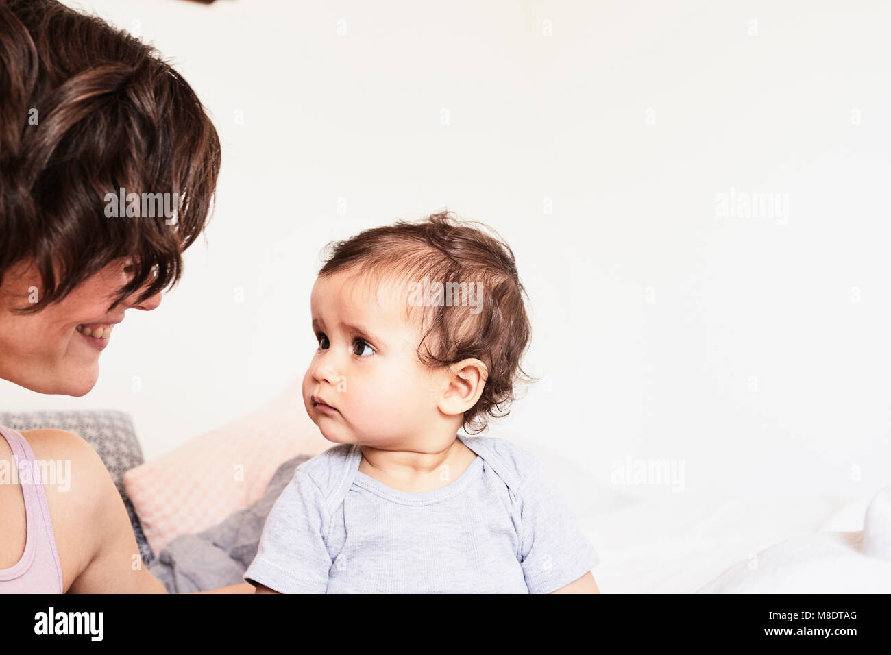 Mother sitting face to face with baby daughter, baby daughter with sad expression Stock Photo