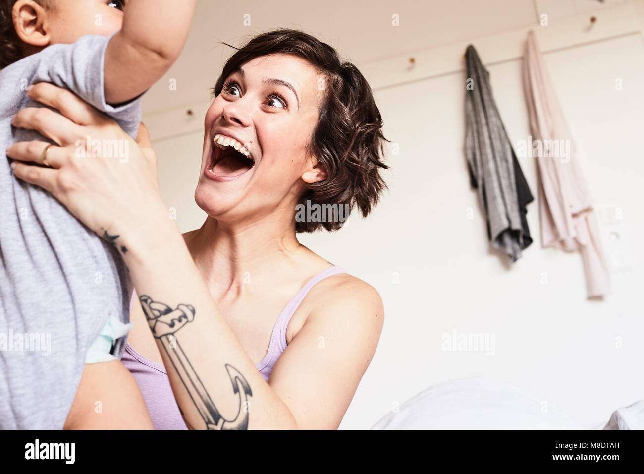 Mother holding baby daughter, face to face, excited expression Stock Photo