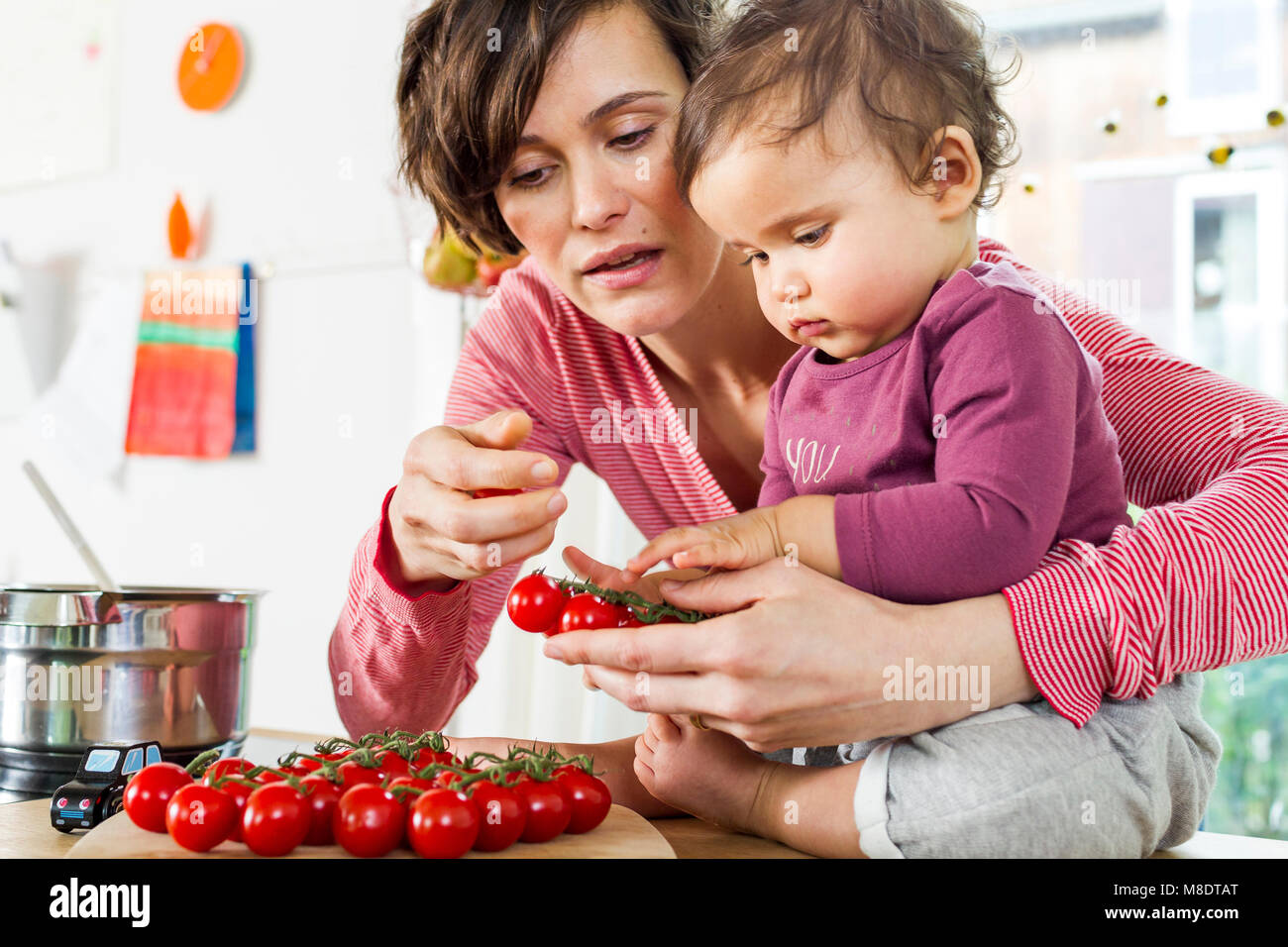 Mother and baby daughter in kitchen, sorting through tomatoes on kitchen counter Stock Photo