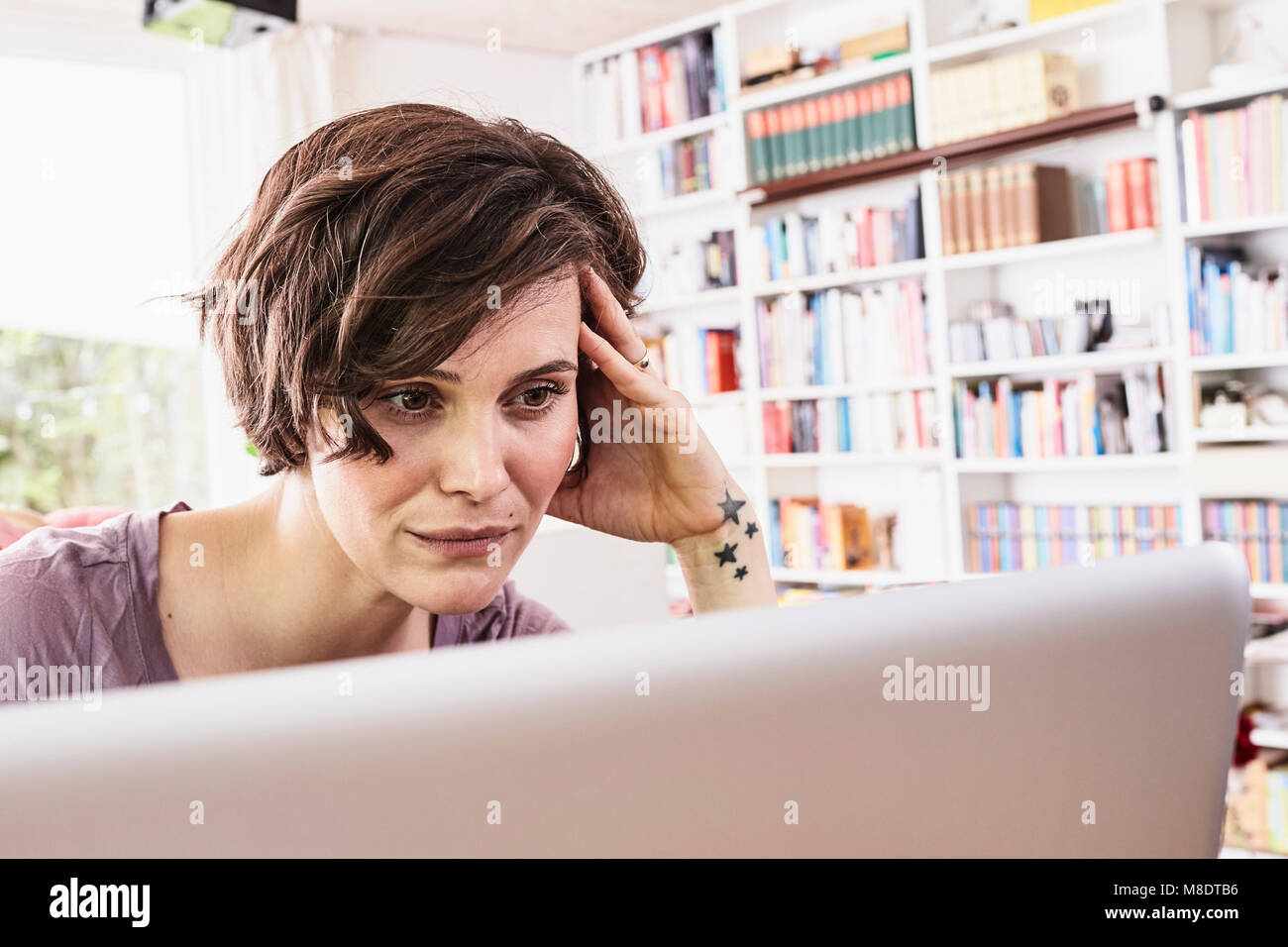 Mid adult woman at home, using laptop, worried expression Stock Photo