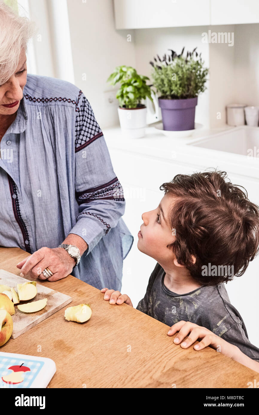 Grandmother and grandson preparing food in kitchen, grandson with questioning expression Stock Photo