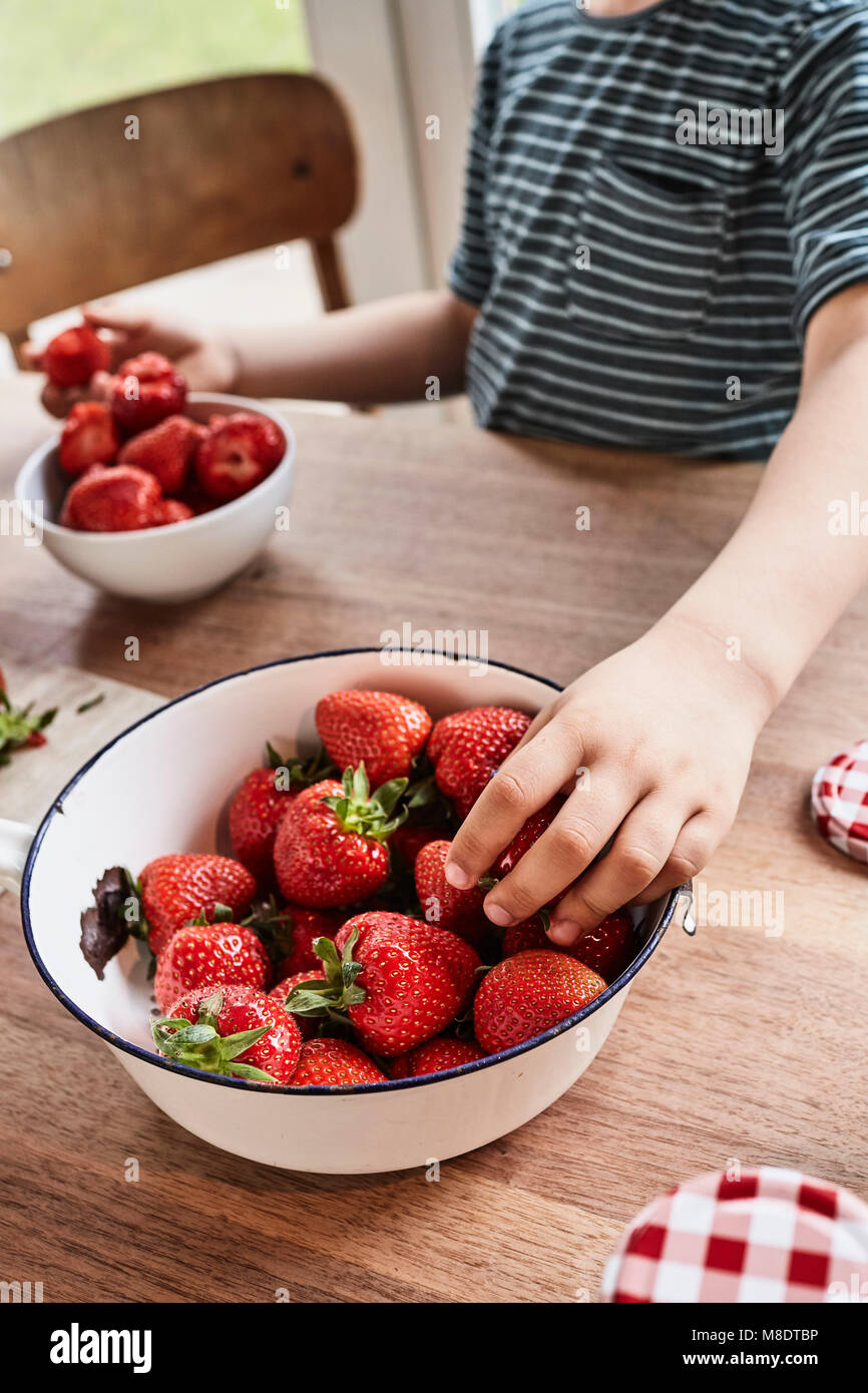 Young boy taking strawberry from bowl, mid section, close-up Stock Photo