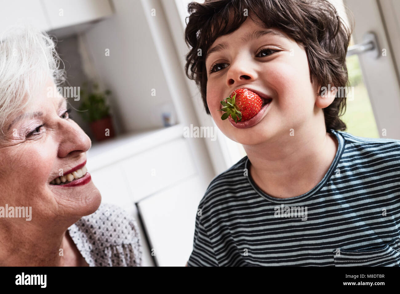 Grandson eating strawberry, grandmother sitting beside him, smiling Stock Photo